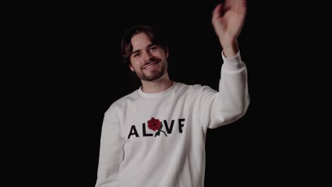 trendy young man waving towards camera, welcoming gesture, wide, black background