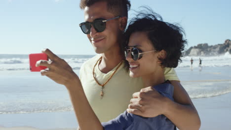 Schönes-Gemischtrassiges-Paar,-Das-Selfies-Macht-Und-Am-Strand-Einen-Kuss-Auf-Die-Wange-Gibt