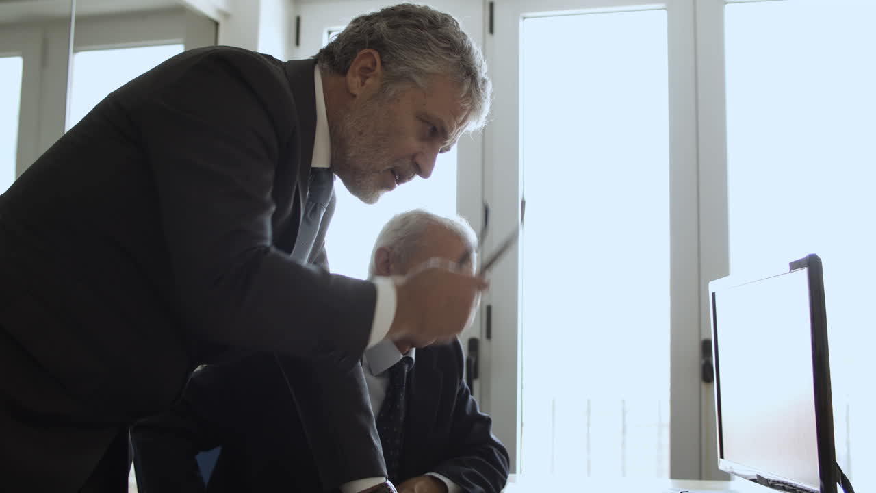 모니터의 콘텐츠에서 펜을 가리키는 두 명의 성숙한 사업가