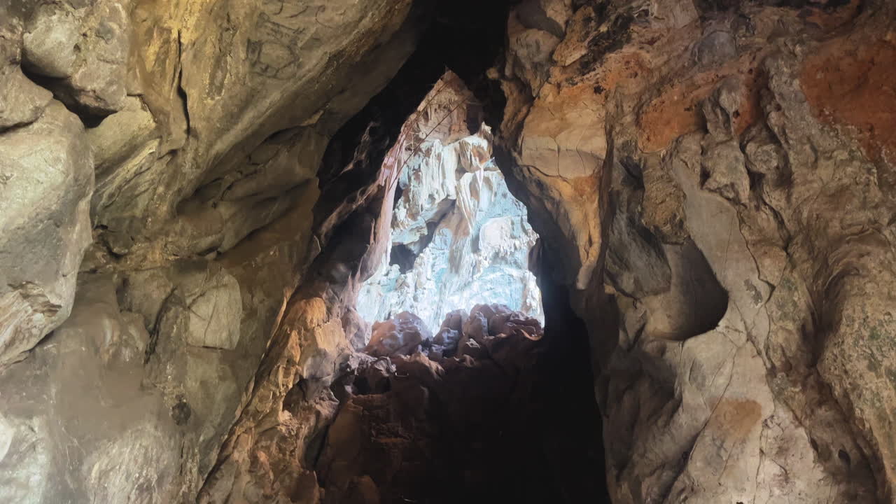 Inside Anxiety State Cave in Chiang Mai, Thailand, towards a distant light source filtering through an opening. Reveals the intricate textures and natural architecture of the cave walls.