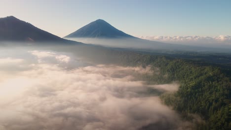 aerial view rising over a misty valley toward volcanic peaks of sunny bali, asia