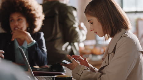 young woman using laptop working in cafe typing email sharing messages on smartphone social media enjoying sitting in busy restaurant