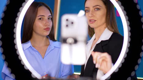 beautiful long-haired brunettes stand behind ring light. women look at the phone camera talking. blogging concept.