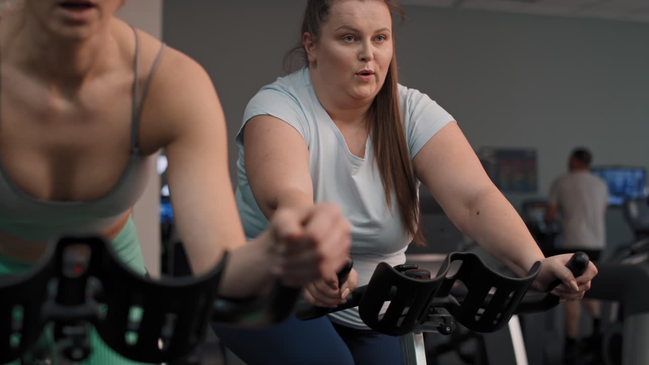 dos mujeres caucásicas montan en bicicleta en el gimnasio.
