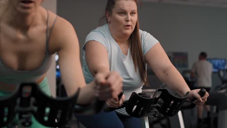 dos mujeres caucásicas montan en bicicleta en el gimnasio.