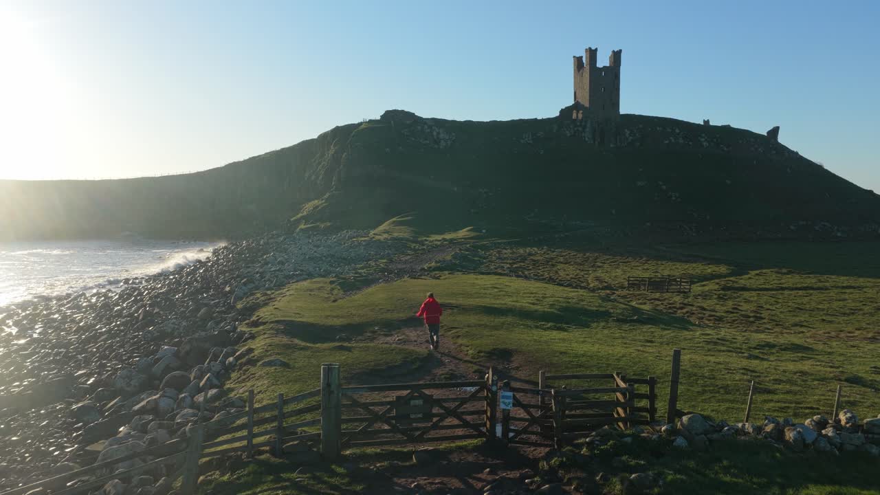 Senderista caminando por la costa hacia el Castillo de Dunstanburgh al amanecer