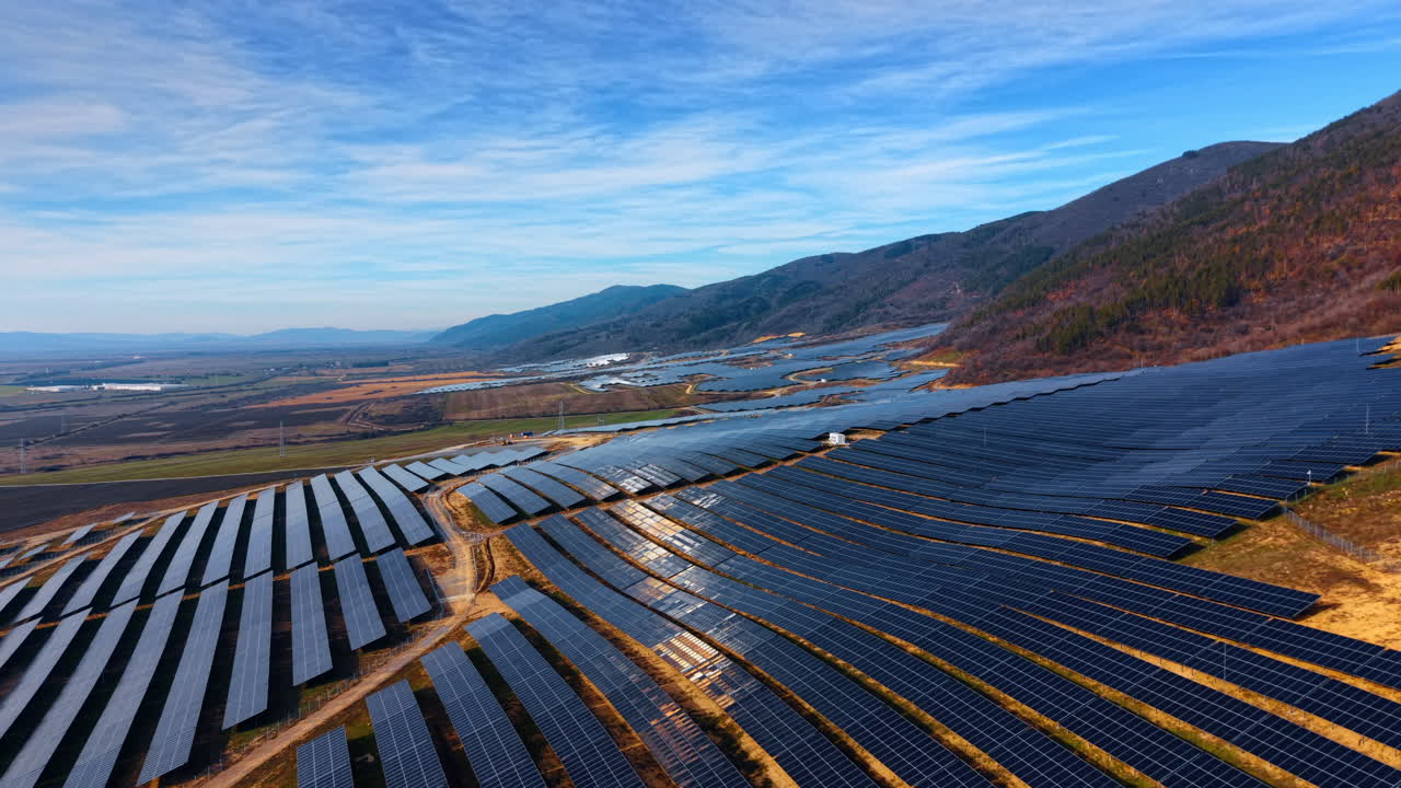 山岳風景に溶け込み太陽光を反射するソーラーパネル発電所。パネルに太陽が反射してきらめき、丘陵を背景にした大規模な太陽光発電設備の空撮。