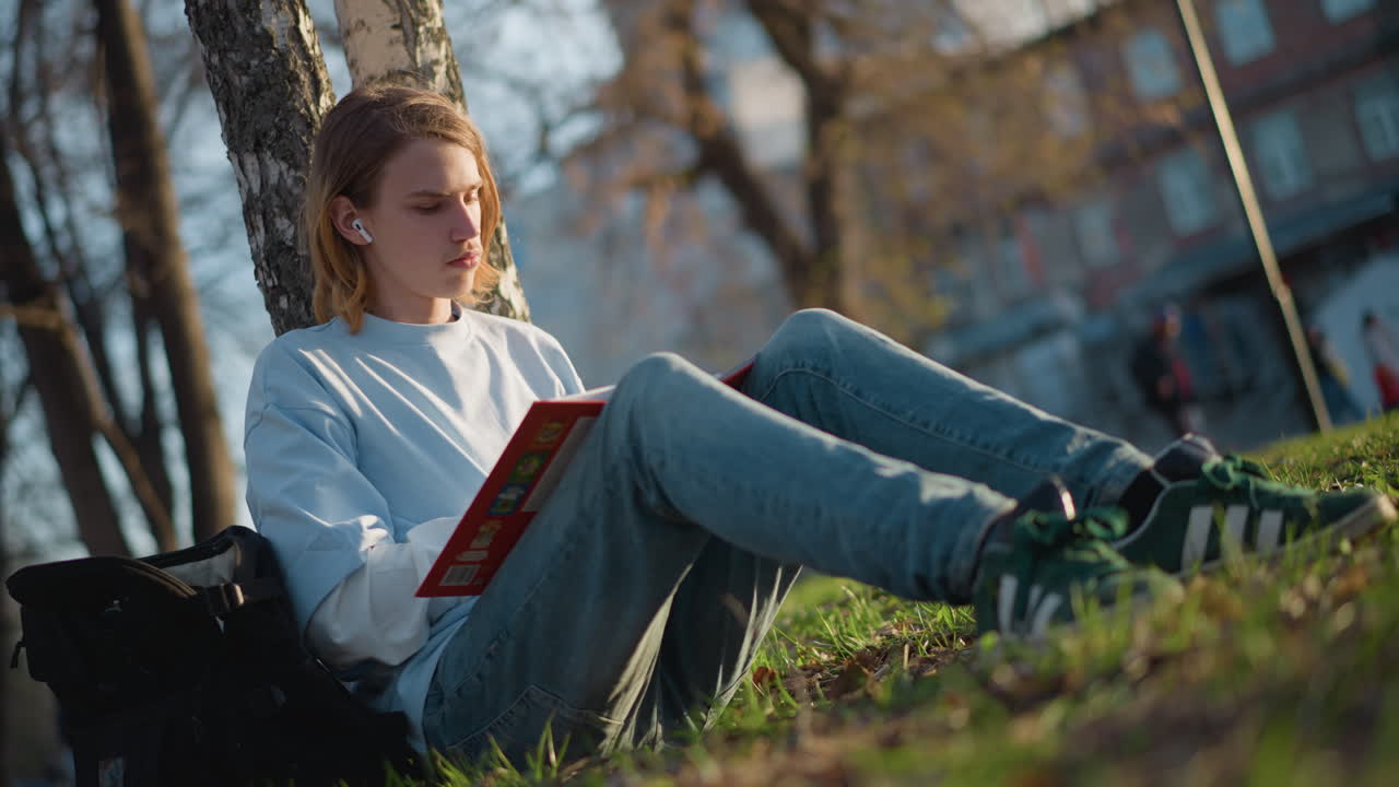 environnement extérieur calme pour la lecture et la prise de notes, analyse de la littérature au calme en plein air dans un environnement herbeux luxuriant, étudiant concentré annote un livre de poche dans un cadre de campus extérieur serein