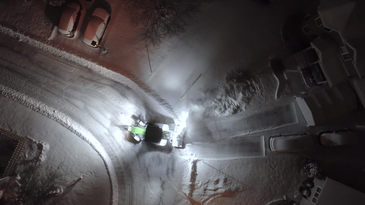 Aerial shot of snow plow clearing out a driveway in St-Constant, Quebec, Canada during the middle of the night with snow covered streets and houses