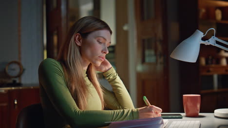 focused student watching online lesson writing in copybook at night home closeup