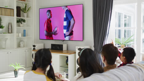 Asiatische-Familie-Vor-Dem-Fernseher-Mit-Verschiedenen-Männlichen-Rugbyspielern-Mit-Ball-Auf-Dem-Bildschirm