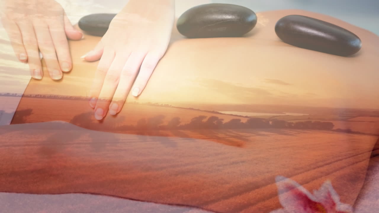 해가 지는 동안 평온한 풍경 위에서 뜨거운 돌로 등을 마사지하는 손