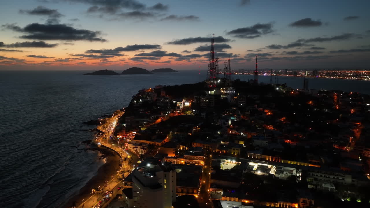 vista aérea orbitando uma colina iluminada na costa de mazatlan, uma noite vibrante no méxico.