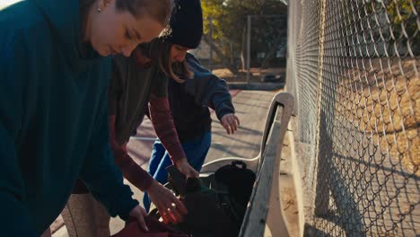 A-trio-of-girls-in-sports-uniforms-put-their-sports-bags-on-a-bench-near-a-lattice-fence-on-a-summer-outdoor-sports-ground-and-prepare-for-basketball-practice-in-the-afternoon