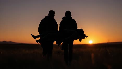 two people carrying another person's silhouette against a sunset