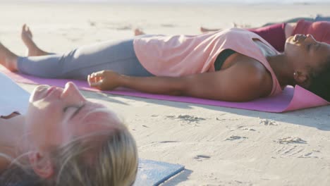 Grupo-De-Amigas-Diversas-Practicando-Yoga,-Tumbadas-En-Colchonetas-En-La-Playa