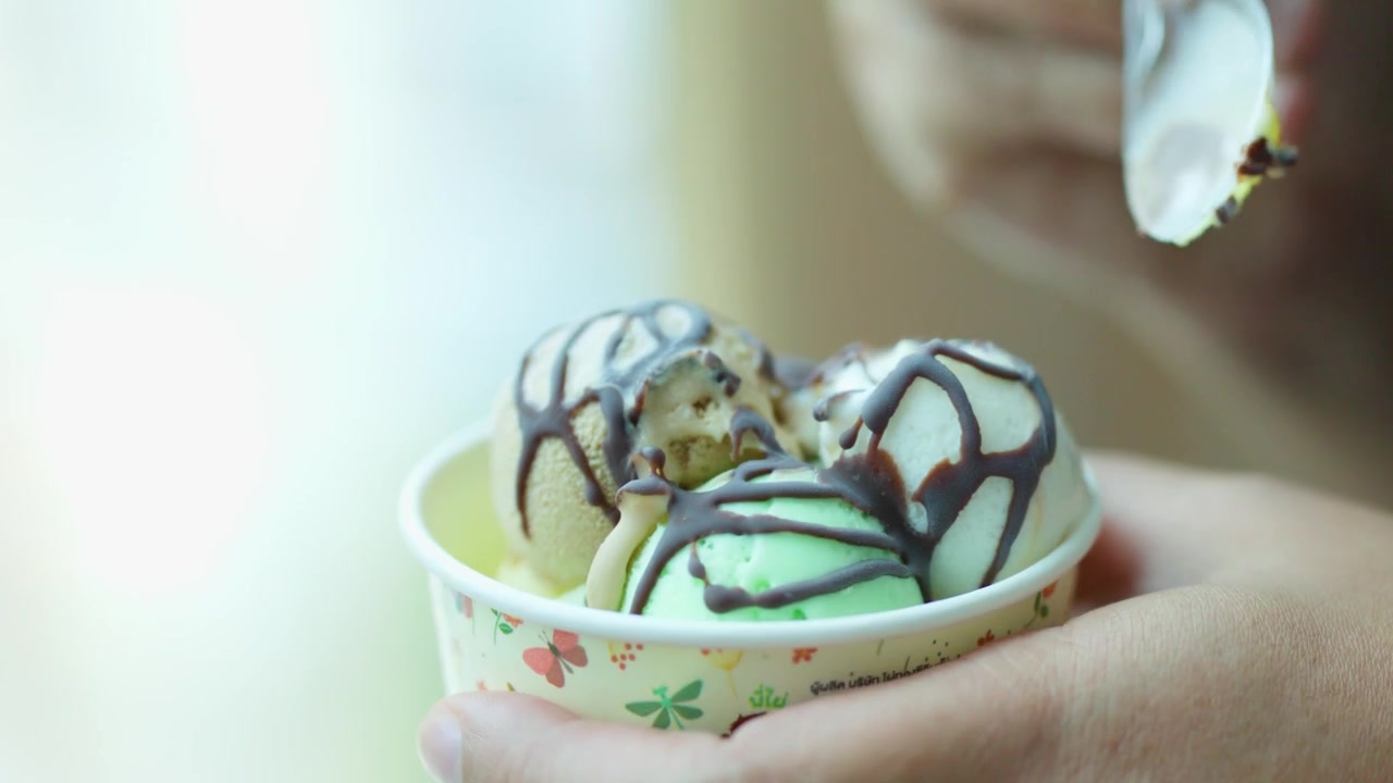 Primo piano di mani che raccolgono gelato assortito con glassa al cioccolato da un bicchiere di carta.