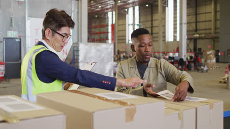 diverse male workers with clipboard and boxes talking in warehouse