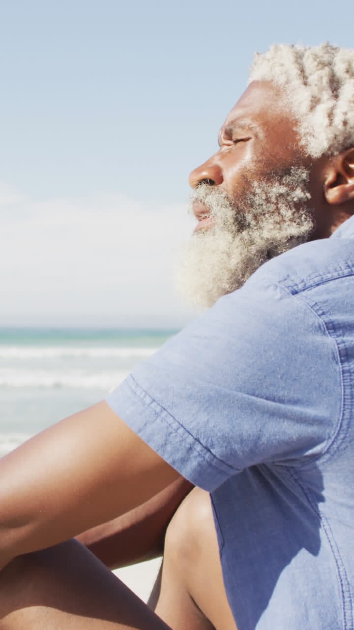 senior afro-amerikaanse man zit en kijkt weg op een zonnig strand
