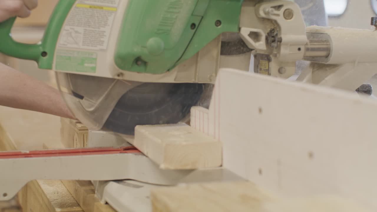 Man using a miter saw to cut a piece wood with video moving on a dolly in slow motion.