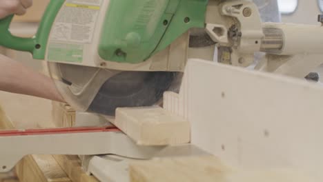 man using a miter saw to cut a piece wood with video moving on a dolly in slow motion.