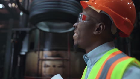 Joyful-man-engineer-smiling-at-huge-modern-factory-wearing-safety-uniform.