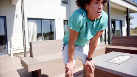 un joven biracial está respirando después de un entrenamiento en el patio trasero de su casa