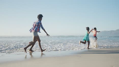 Glückliches-Afroamerikanisches-Paar-Läuft-Mit-Tochter-Und-Sohn-Am-Sonnigen-Strand