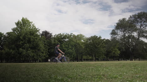 a man bikes from left to right across a green field with trees in background