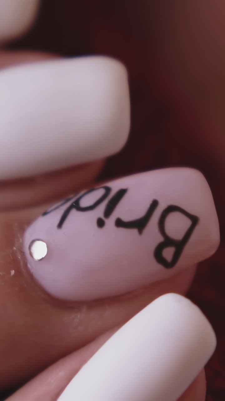 CU, slow motion: stylish young woman holds gentle hand with beautiful pink and white manicure with word bride on nail on blurred background closeup