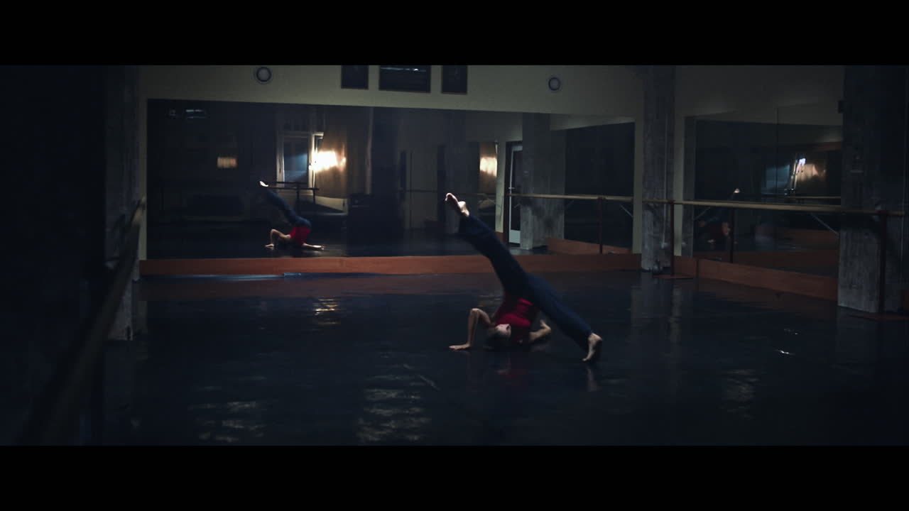A young woman practices modern dancing and ballet in a moody room full of mirrors