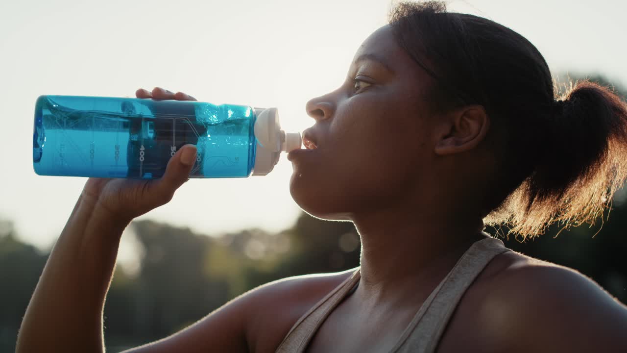 mujer bebiendo agua durante el entrenamiento en el parque.