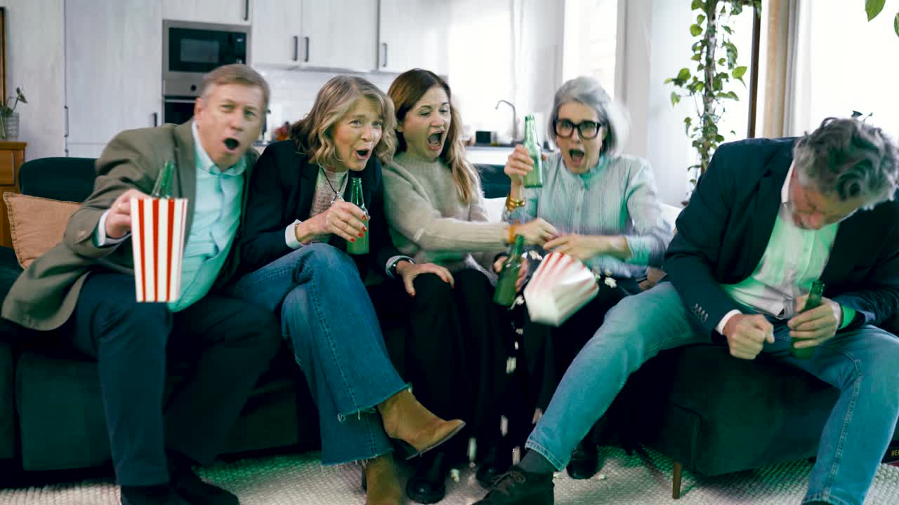 Upprymd grupp vänner som tittar på TV och firar hemma