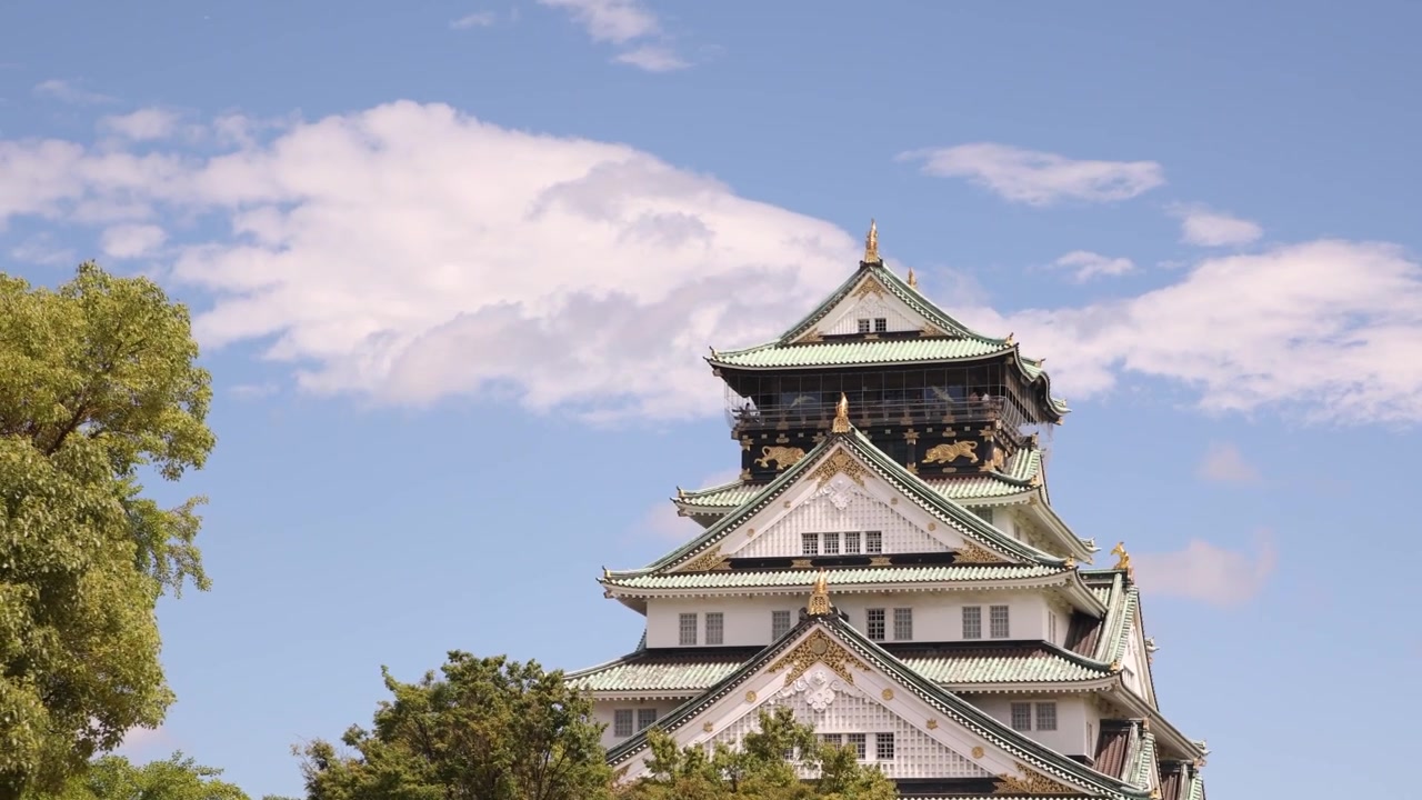 Vista dell'iconica torre principale del Castello di Osaka in Giappone, che si erge sopra gli alberi circostanti e mostra la tradizionale architettura delle fortezze giapponesi sotto un cielo luminoso