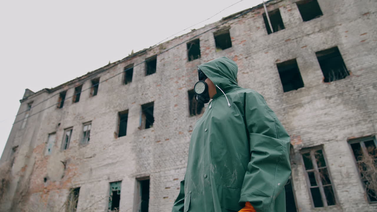 Consequences of chemical attack in the city. Human in safety suit and mask to breathe standing alone on the background of ruined building without windows.