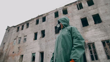 consequences of chemical attack in the city. human in safety suit and mask to breathe standing alone on the background of ruined building without windows.