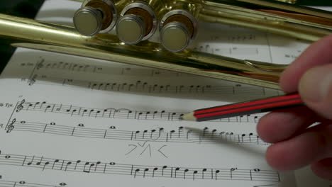 a composer making notes on a piece of sheet music with a pencil with a brass trumpet in the background