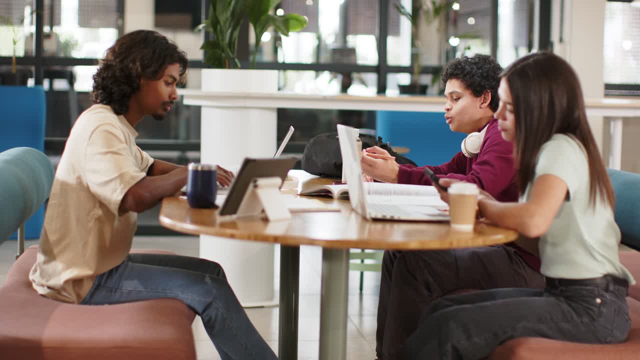 African American students studying at lounge table, center holding paper sparking talk with laptops