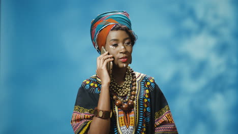 joven afroamericana hermosa mujer con ropa tradicional y turbante hablando por teléfono inteligente