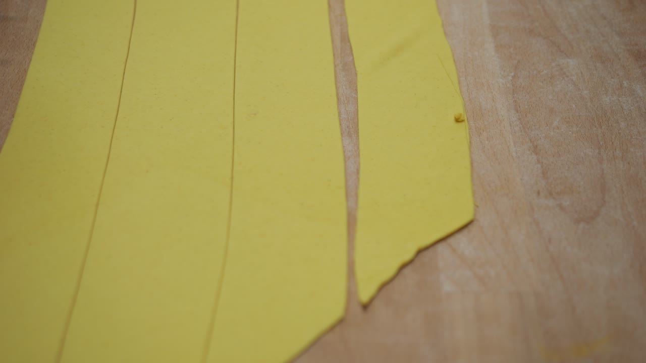 Professional chef preparing fresh tortelli and tagliatelle pasta dough at a wooden counter, using a hand cutter for traditional Italian cuisine in a restaurant kitchen