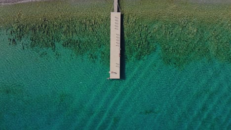 Solo-person-walks-along-wooden-deck-to-edge-enjoying-blue-mediterranean-waters-at-edge-dropoff,-aerial-bird's-eye-view