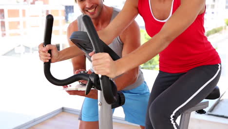 Mujer-En-Forma-Trabajando-En-Bicicleta-Estática-Con-Su-Entrenador