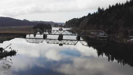 low-level-flight-over-Siuslaw-river-and-old-rail-bridge-in-the-town-of-Cushman,-OR,-USA