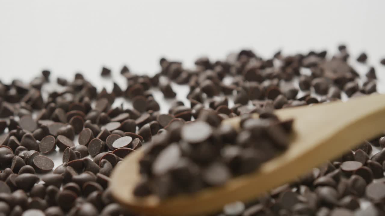 Video of close up of multiple chocolate chip falling on wooden spoon over white background
