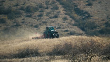 Vista-De-Teleobjetivo-De-Un-Tractor-Arando-En-Un-Campo-En-Un-Día-Cálido-Y-Soleado-Con-Una-Colina-En-El-Fondo