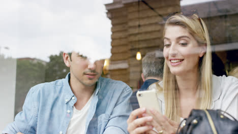 Amigos-Usando-Teléfonos-Inteligentes-Mostrando-Conectividad-En-Un-Café-Sonriendo-A-Cámara-Lenta