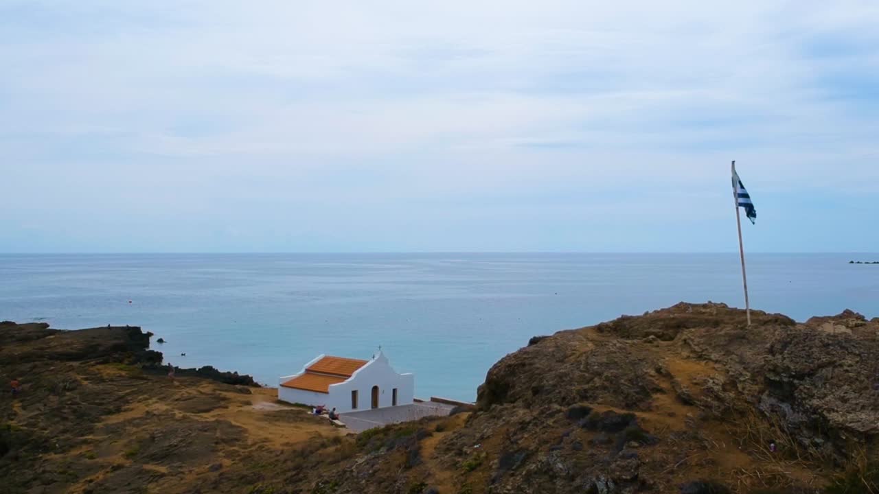 Greek flag on top of Point St. Nicholas at the far east of the Zakynthos Island in Greece, Aerial drone flyover shot on overcast sky