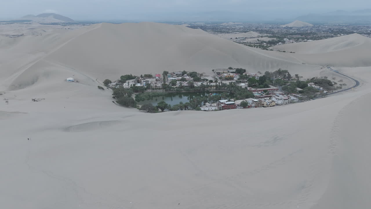Drone shot revealing the city of Huacachina in Peru behind the dunes on a cloudy day LOG