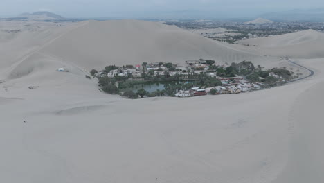 drone shot revealing the city of huacachina in peru behind the dunes on a cloudy day log