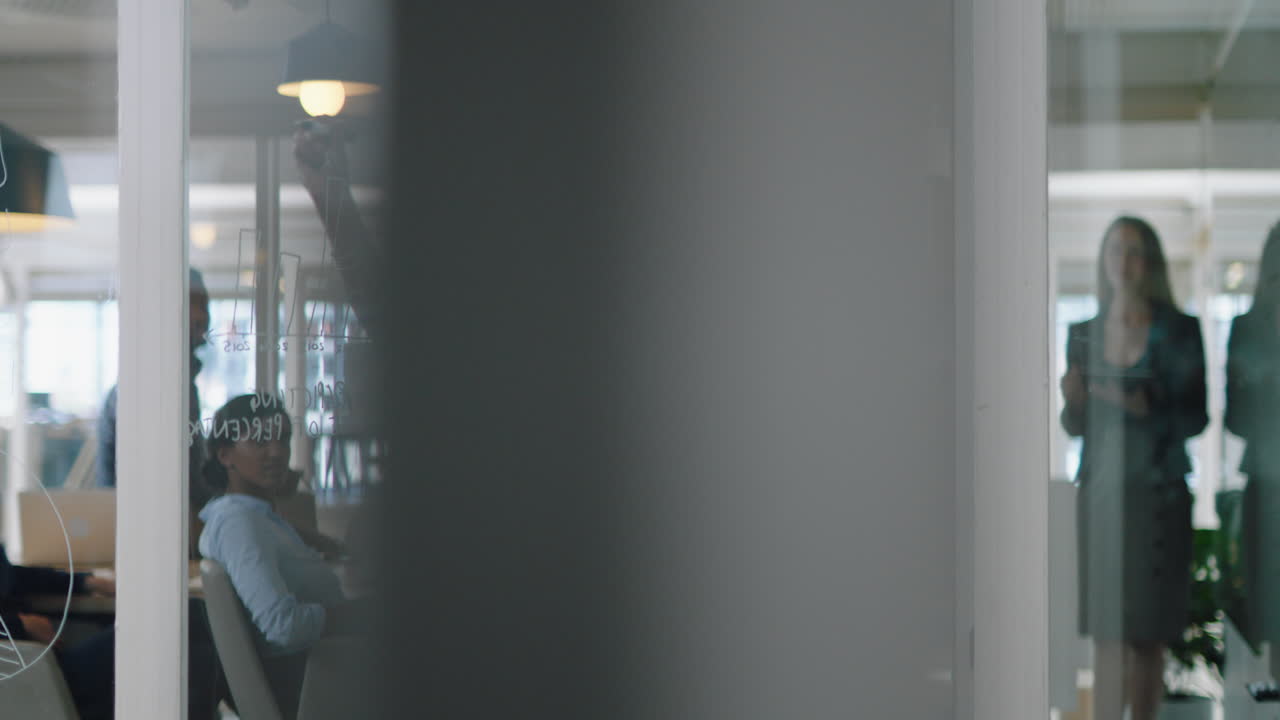 joven mujer de negocios de raza mixta escribiendo en una pizarra de vidrio líder de equipo entrenando a colegas en reuniones lluvia de ideas estrategia de resolución de problemas compartiendo ideas en la oficina seminario de presentación 4k